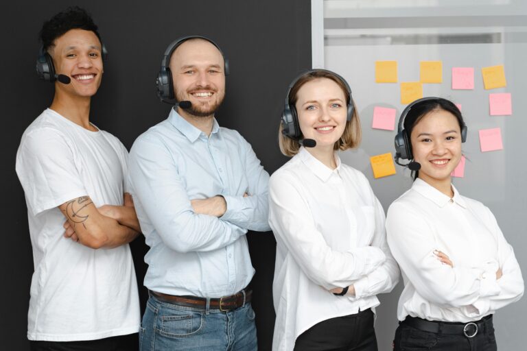 Team of diverse call center professionals smiling and standing confidently with headsets and microphones.