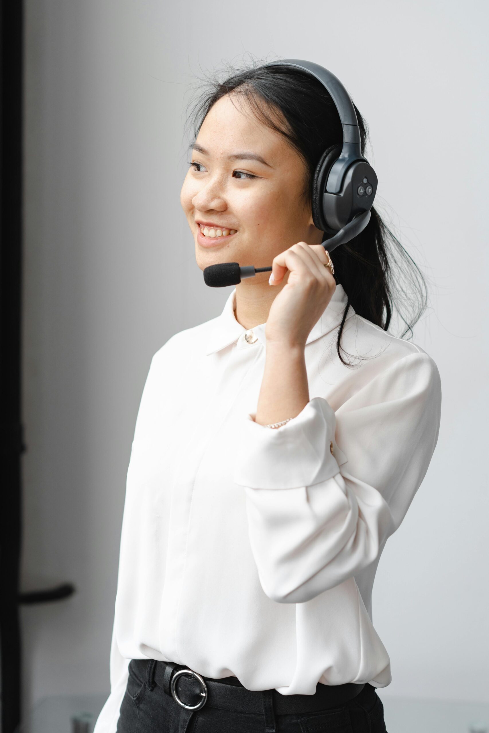 Smiling Asian woman with headset providing customer support in an office setting.